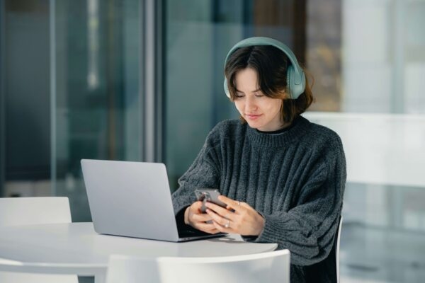Woman on phone with laptop in view wearing headphones